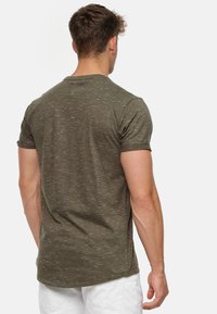 Olivgrünes Kurzarm-T-Shirt mit einem strukturierten, gesprenkelt gestalteten Design. Gerader Saum und Rundhalsausschnitt. Das Material wirkt weich und leicht.