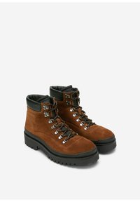 Braune Wildleder-Wanderschuhe mit schwarzen Gummisohlen, ausgestattet mit Metallösen, schwarzen Schnürsenkeln und gepolsterten Kragen für zusätzlichen Komfort.