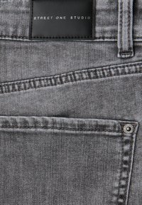 Graue Denim-Hose mit einem schwarzen Lederetikett, auf dem "STREET ONE STUDIO" steht. Mit gestickten Details und einem Metallknopf an der Tasche.