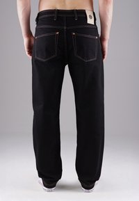 Černé džíny z denimu s přímým střihem, zdobené měděnými kovovými doplňky, zadními kapsami a kontrastním prošitím. Kombinovány s bílými teniskami.