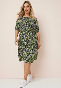 Musta polvipituinen kukkamekko, jossa on violetit ja keltaiset kukat, lyhyet puff-hihat ja rento istuvuus. Yhdistetty valkoisiin lenkkareihin.