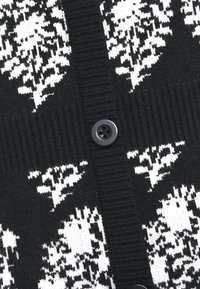 Cardigan en maille noire avec motifs floraux blancs, texture côtelée et un bouton rond noir au centre avant.