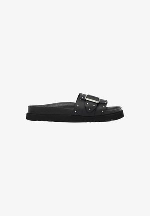 Black slide sandal with a thick sole, studded leather strap, and large silver buckle on a white background.