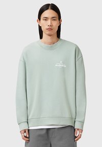 Sudadera verde claro con cuello redondo, mangas anchas y puños acanalados. Presenta un pequeño logo blanco en el pecho, hecha de material suave.