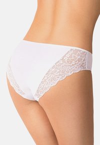 Mutandine di cotone bianco con bordo in pizzo ai lati, texture liscia e taglio a slip classico. Dettagli accentuati da pizzo floreale.