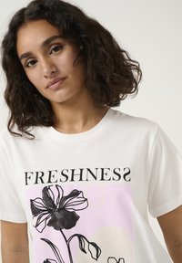 T-shirt blanc avec un design graphique floral en noir et des accents roses. "FRAÎCHEUR" est imprimé en lettres noires en gras au-dessus du design.
