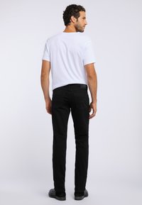 Czarne dżinsy o slim fit i pięciu kieszeniach, w połączeniu z gładką białą koszulką. Model stoi plecami, ukazując subtelne detale szwów.