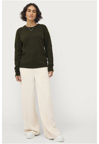 Maglione lavorato a maglia di un verde scuro con scollatura a girocollo, abbinato a pantaloni a gamba larga beige chiaro e sneakers bianche. Design semplice, tessuto testurizzato.