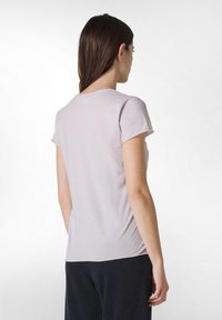 Camiseta corta de manga corta en púrpura claro con un escote redondo y una textura suave. La vista posterior muestra un diseño ajustado y un dobladillo ligeramente curvado.