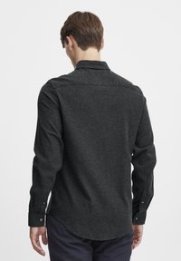 Menns langermet skjorte i mørk grått stoff. Den har en krage med knapper og knappefester ved mansjettene, med en buet nederkant og teksturert finish.