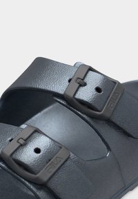 Gros plan sur les brides de sandale noires Fila avec boucles noires mates réglables et finition texturée sur un fond clair.