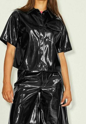 Woman wearing shiny black short-sleeve button-up shirt with matching high-waisted wide-leg pants against plain background.