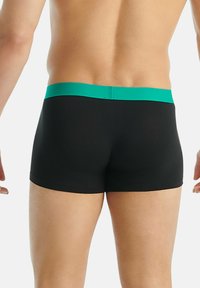 Shorts de bain noirs avec une ceinture texturée verte, offrant une coupe ajustée et un tissu doux, adaptés à un usage athlétique.