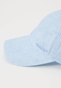 Világoskék sapka texturált anyagból, ívelt napellenzővel és a GANT logójával hímezve az oldalán.