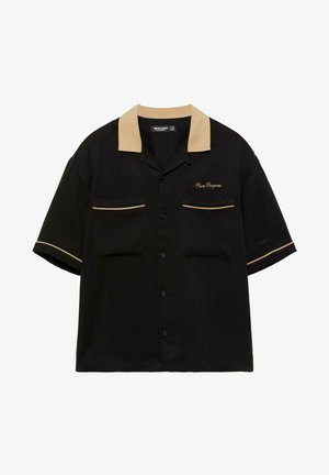 Zwart kortärmlig overhemd met knopen, beige kraag, beige bies op zakken en mouwen, en 'Pure Purpose' geborduurd op de linkerborst.