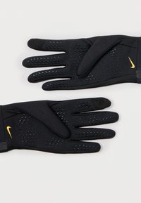 Mănuși negre cu prindere texturată, având logo-ul galben Nike. Fabricate din material flexibil, cu perforații pentru ventilație și o potrivire strânsă.