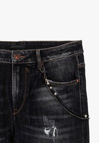 Donkerdenim jeans met een versleten uitstraling, contrasterende stiksels en een decoratieve ketting met kralen en metalen accenten die aan de tailleband zijn bevestigd.