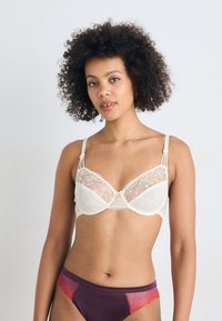 Bralet z žico v kremni barvi iz satena in čipke, ki ima cvetlične vzorce in nežne naramnice. Ujemajoče se vijolične hlačke z čipkastimi detajli.