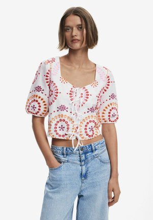 Blusa bianca corta con ricami floreali colorati in rosa, arancio e rosso; presenta una scollatura quadrata e dettagli con lacci frontali.