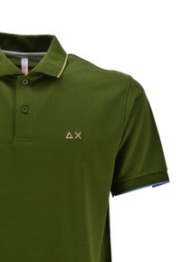 Polo verde con colletto e maniche corte. Include un logo con forme geometriche bianche. Colore di accentuazione sui bordi delle maniche.