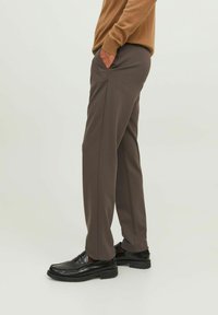 Tmavě hnědé kalhoty s hladkou texturou, vybavené bočními kapsami a střihem s rovnými nohavicemi, doplněné černými mokasíny.