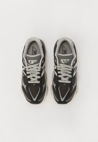 Sneaker neri e grigi con tomaia in mesh e suede, punta rotonda, suola in gomma spessa e accenti a contrasto con un logo riflettente.