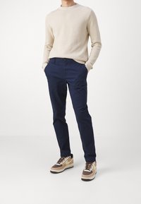 Navy bomullbyxor, figursydd design, fyra fickor, kombinerade med en beige strukturerad tröja och bruna samt beige sneakers med logotypdetaljer.