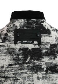 Tela abstracta en blanco y negro con una superficie texturada. Presenta un cuello de pana negro y una etiqueta rectangular con botones.