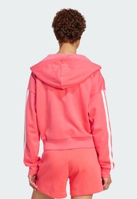 Koral sweatshirt med hette, med hvite sidestriper og ribbet mansjetter, sammen med matchende koralshorts. Myk, strukturert stoff.
