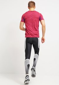 Ropa deportiva que presenta una camiseta ajustada de manga corta en un degradado rojo, combinada con legging negros que muestran patrones de olas blancas y zapatillas deportivas.