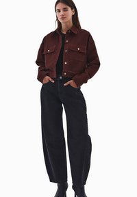 Burgundowa kurtka z żakardowej tkaniny o kroju krótkim, z dwiema kieszeniami na piersi, srebrnymi guzikami i luźnym fasonem, w zestawieniu z czarnymi dżinsami o wysokim stanie.