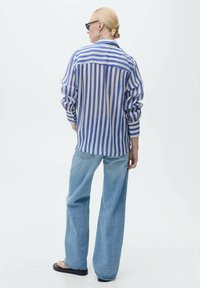 Gestreifte Bluse in Blau- und Cremetönen, lockere Passform, mit Knopfleiste und langen Ärmeln, kombiniert mit hellblauen weiten Jeans.