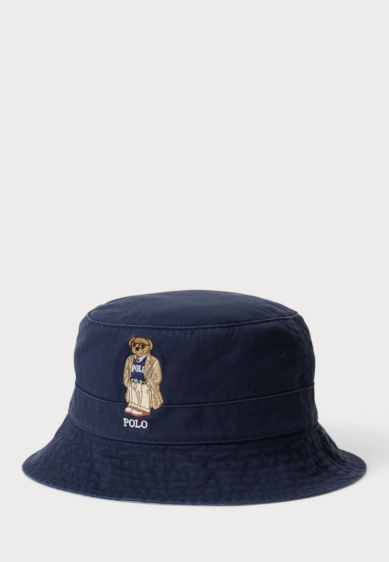 Chapeau seau bleu marine en coton, avec un tissu texturé et un ours brodé en crème portant le mot "POLO."
