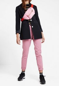 Svart skräddarsydd kappa med vit söm, rosa midjeväska, randig skjorta, rosa byxor och svarta sneakers med vita accenter.