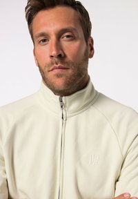 Chaqueta de forro polar de cremallera ligera con cuello alto; presenta un logo en el pecho, textura suave y costuras planas para un acabado limpio.