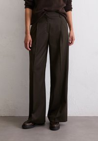 Pantalons à taille haute et jambes larges en tissu marron foncé avec des plis à l'avant et des poches latérales, associés à des chaussures marron foncé.