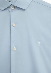 Light blue button-up shirt with a collar, three visible buttons, and small white embroidered figure playing polo on the chest.