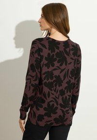 Pull à manches longues en prune foncé avec un motif floral noir, présentant un col rond et des poignets côtelés. Le tissu semble élastique et texturé.