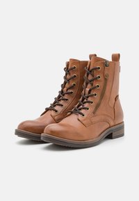 Bottines en cuir marron avec fermeture à lacets et zip, bout rond et surface texturée. Talon court et tirette sur le côté pour un enfilage facile.