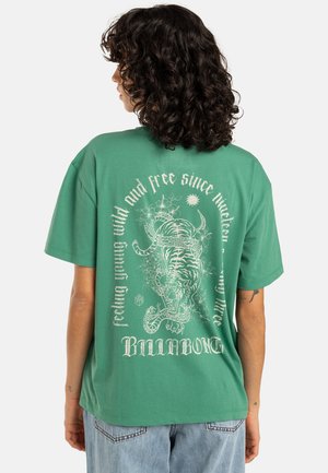 Groene oversized t-shirt van katoen, met een witte tijgerafbeelding op de achterkant, omringd door tekst en decoratieve elementen.