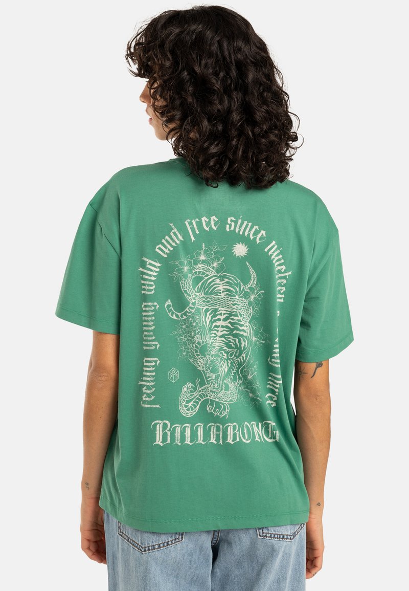 Camiseta verde de gran tamaño hecha de algodón, con un gráfico de un tigre en blanco en la parte posterior, acompañado de texto y elementos decorativos a su alrededor.