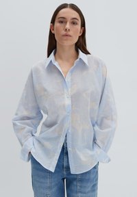 Camicetta azzurro chiaro, con bottoni, in tessuto trasparente con motivi astratti color crema. Presenta un colletto classico e maniche lunghe e larghe.
