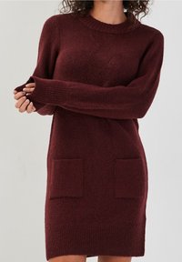 Robe pull en tricot bordeaux avec un col côtelé, des manches longues et deux poches avant avec un motif texturé.