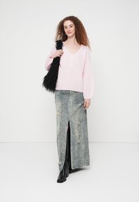 Χοντρό ροζ πλεκτό πουλόβερ με λαιμόκοψη σε σχήμα V, συνδυασμένο με γκρι μάξι φούστα με τύπωμα φιδιού, με σκίσιμο μπροστά και φθαρμένες λεπτομέρειες. Μαύρες μπότες με τακούνι.