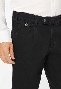 Schwarze Hosen aus einem Baumwollmischgewebe. Verfügt über einen Knopfverschluss, seitliche und vordere Taschen sowie eine gesteppte Optik entlang der Nähten.