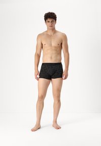 Fekete mintás boxer alsónadrág, amely szoros illeszkedésű és puha derékrésszel rendelkezik. Az anyag simának tűnik, finom textúrával. A lábak mezítelenek.