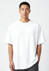 Biela tričko s okrúhlym výstrihom vyrobené z bavlny, s krátkymi rukávmi, vo voľnom strihu a hladkej textúre, doplnené o šedé šortky.