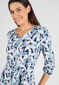 Blaues und grünes Blumendruckkleid mit Dreiviertelärmeln, V-Ausschnitt und gebundenem Bund. Der Stoff hat eine glatte Textur.