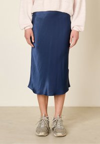 Jupe glissante en satin marine avec une texture lisse, longueur genoux, associée à des baskets gris clair. Le design est simple avec un ourlet arrondi.