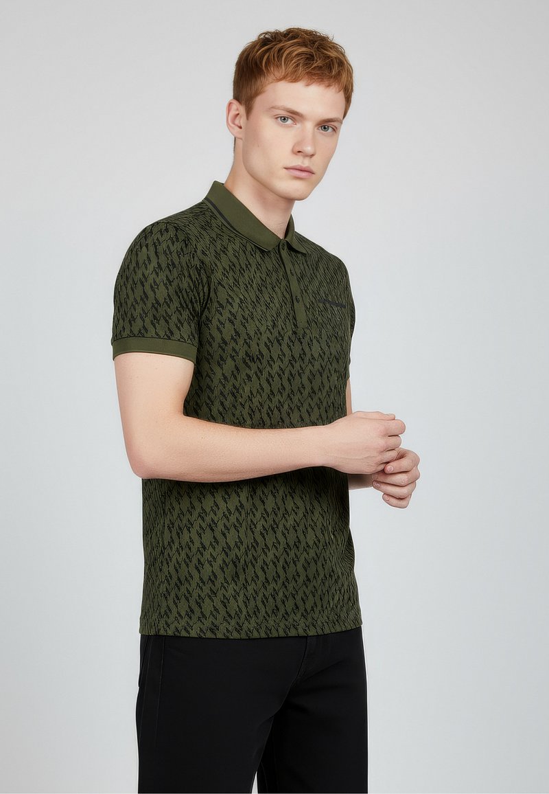 Zelené polo tričko s texturovaným cikcak vzorem, krátkými rukávy a límečkem. Černé detaily na hrudníku. Nošeno s černými kalhotami.